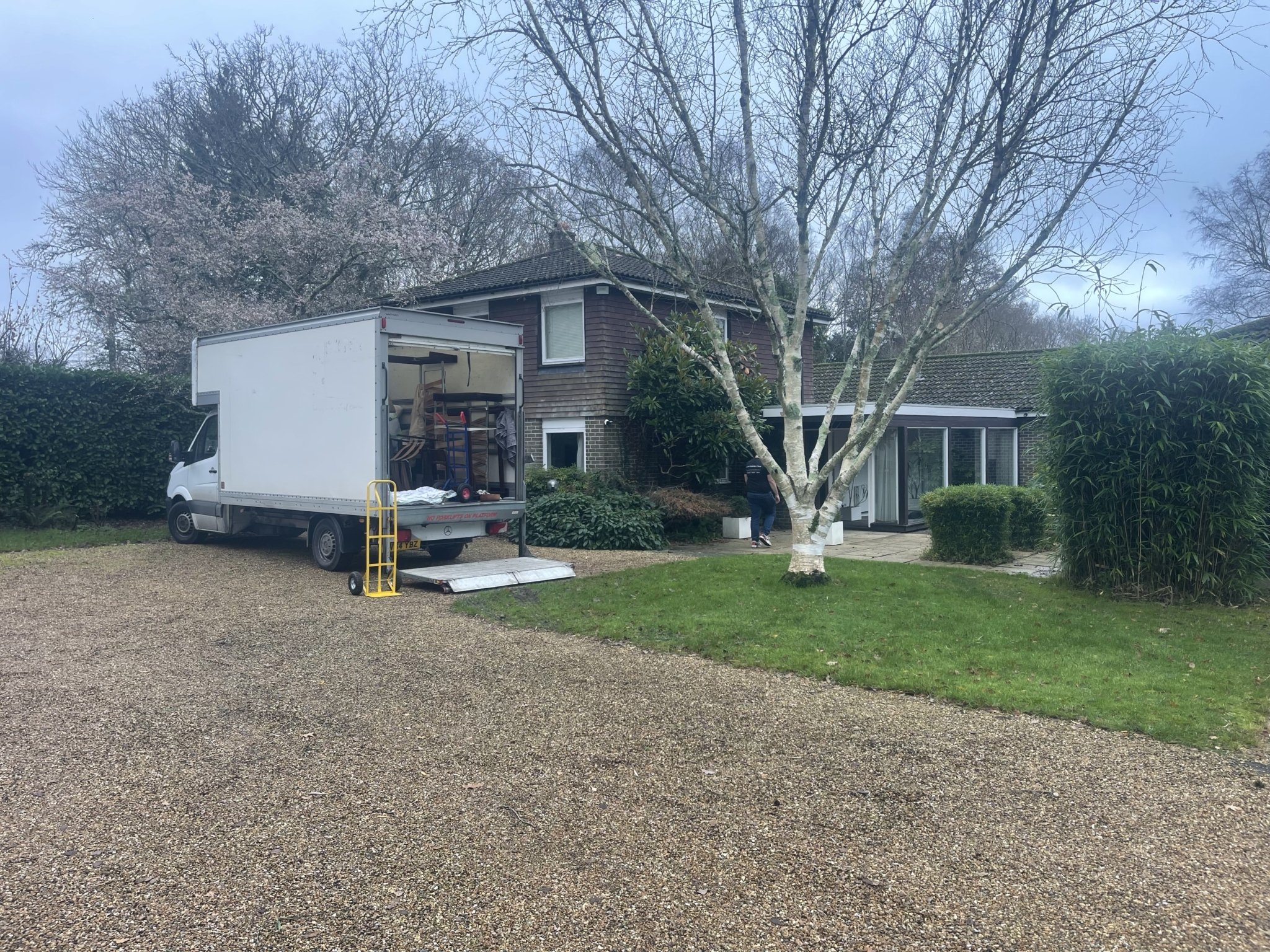 ESV Removals Luton van parked on a gravel driveway outside a house in winter, with the rear ramp down and a trolley beside it, showing a December move setup with wet weather and muddy ground.