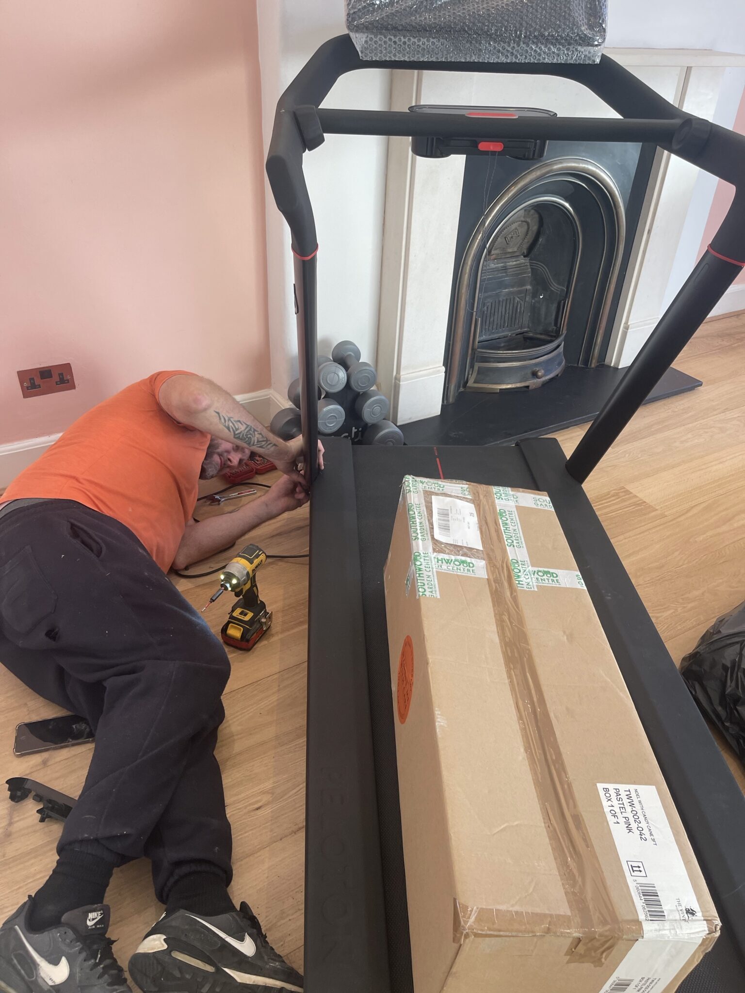 Close up of an ESV Removals fitter lying beside a treadmill, tightening bolts with tools during post move assembly work.