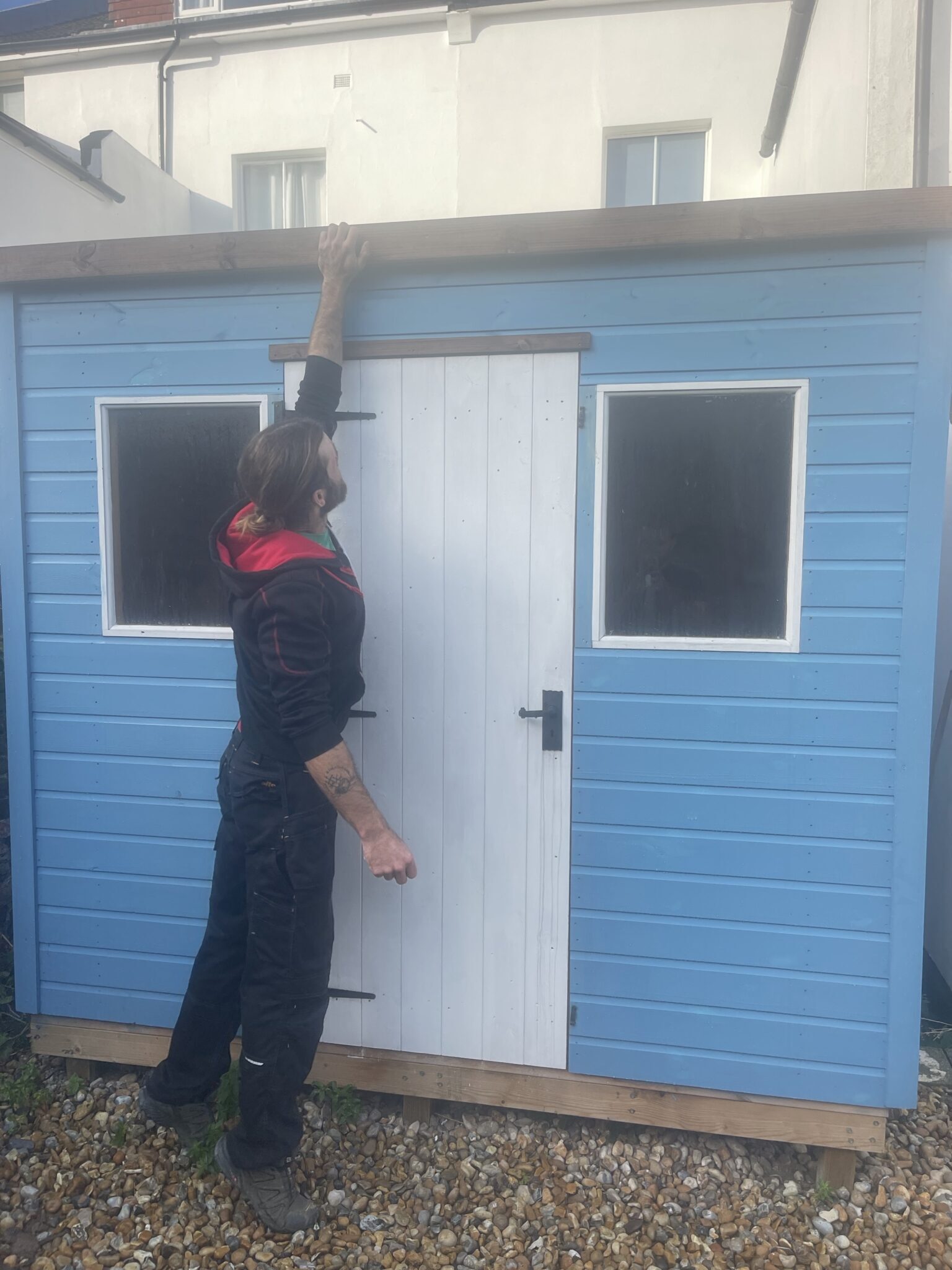 Handyman checking roof line and felt before dismantling a blue timber shed in Brighton